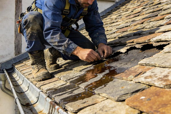 Technicien inspectant les infiltrations d'eau sous les ardoises du toit